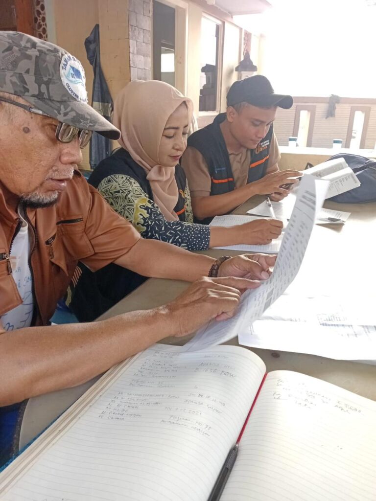 Three people at a table outside a building review documents together elderly man in camo cap woman in hijab and a young person in a vest